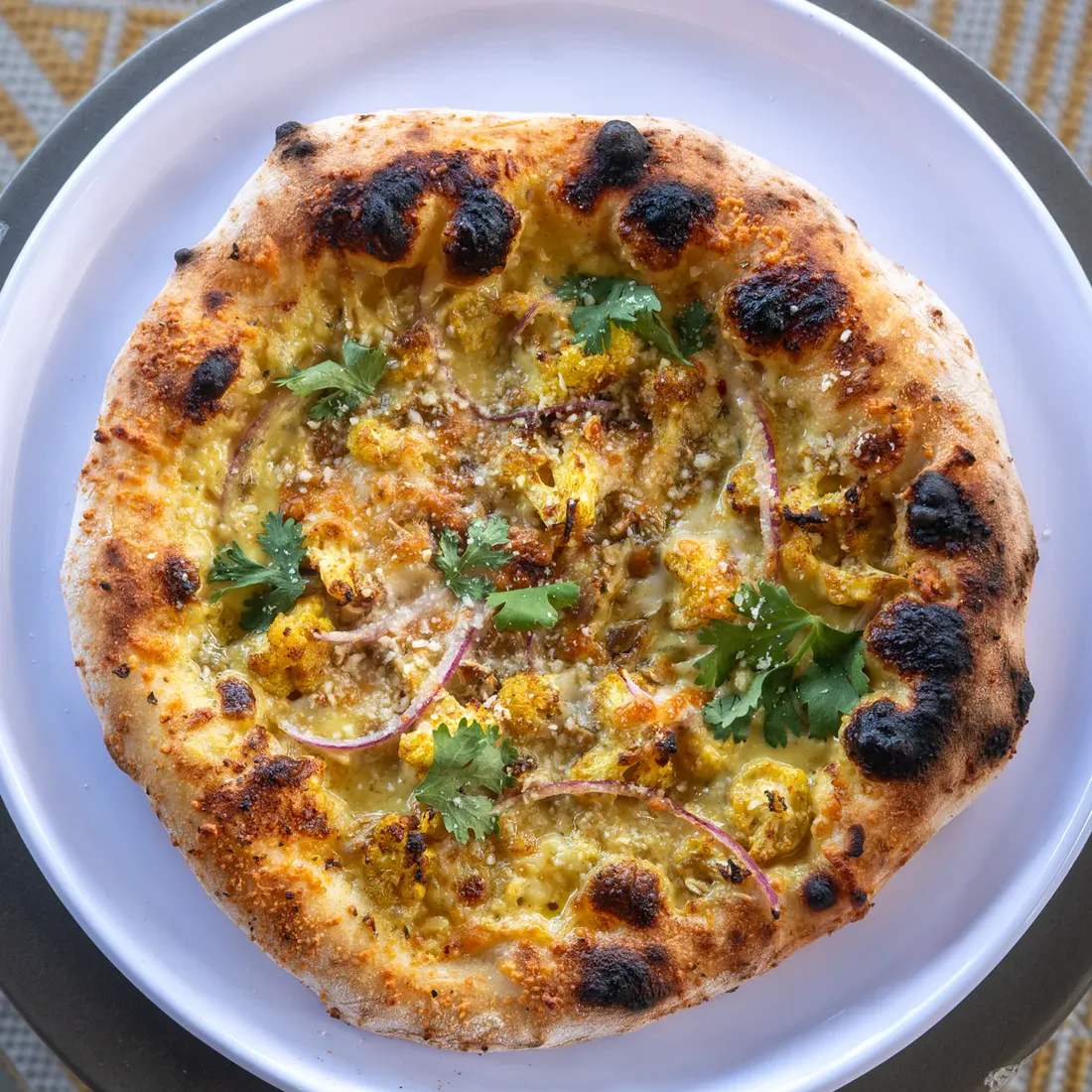 Crust's Curried Cauliflower pizza with roasted cauliflower, red onion, pepitas, and cilantro.