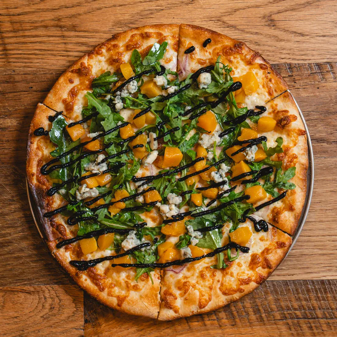 Goodfella's Southern Hitman pizza with onions, peaches, arugula, Gorgonzola, and balsamic drizzle.